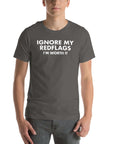 Man wearing asphalt “IGNORE MY RED FLAGS I’M WORTH IT” t-shirt, standing casually with hands by pockets.