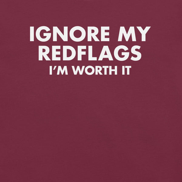 Close-up of maroon t-shirt with bold white text “IGNORE MY RED FLAGS I’M WORTH IT” printed on the front.        