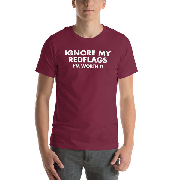 Man wearing maroon “IGNORE MY RED FLAGS I’M WORTH IT” t-shirt, standing casually with hands by pockets.