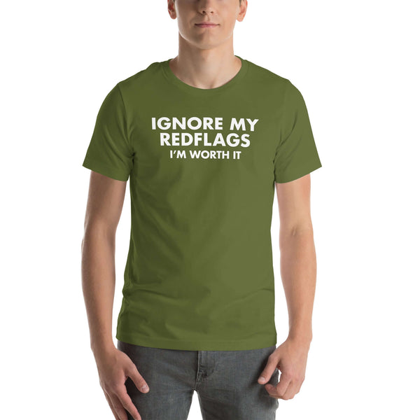 Man wearing olive “IGNORE MY RED FLAGS I’M WORTH IT” t-shirt, standing casually with hands by pockets.