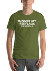 Man wearing olive “IGNORE MY RED FLAGS I’M WORTH IT” t-shirt, standing casually with hands by pockets.