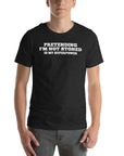 Man wearing black “PRETENDING I’M NOT STONED IS MY SUPERPOWER” t-shirt, standing casually with hands by pockets.