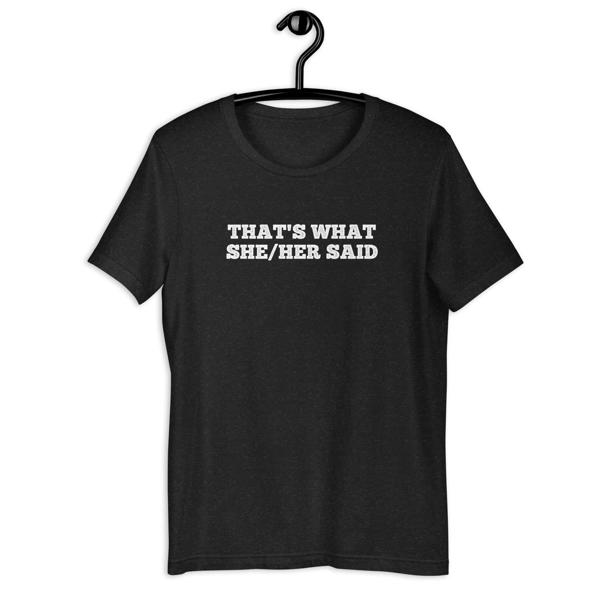 Black “THAT’S WHAT SHE/HER SAID” t-shirt hanging on a hanger, front design visible.      