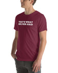 Man wearing a maroon “THAT’S WHAT SHE/HER SAID” t-shirt, standing with hands in pockets, looking to the side.