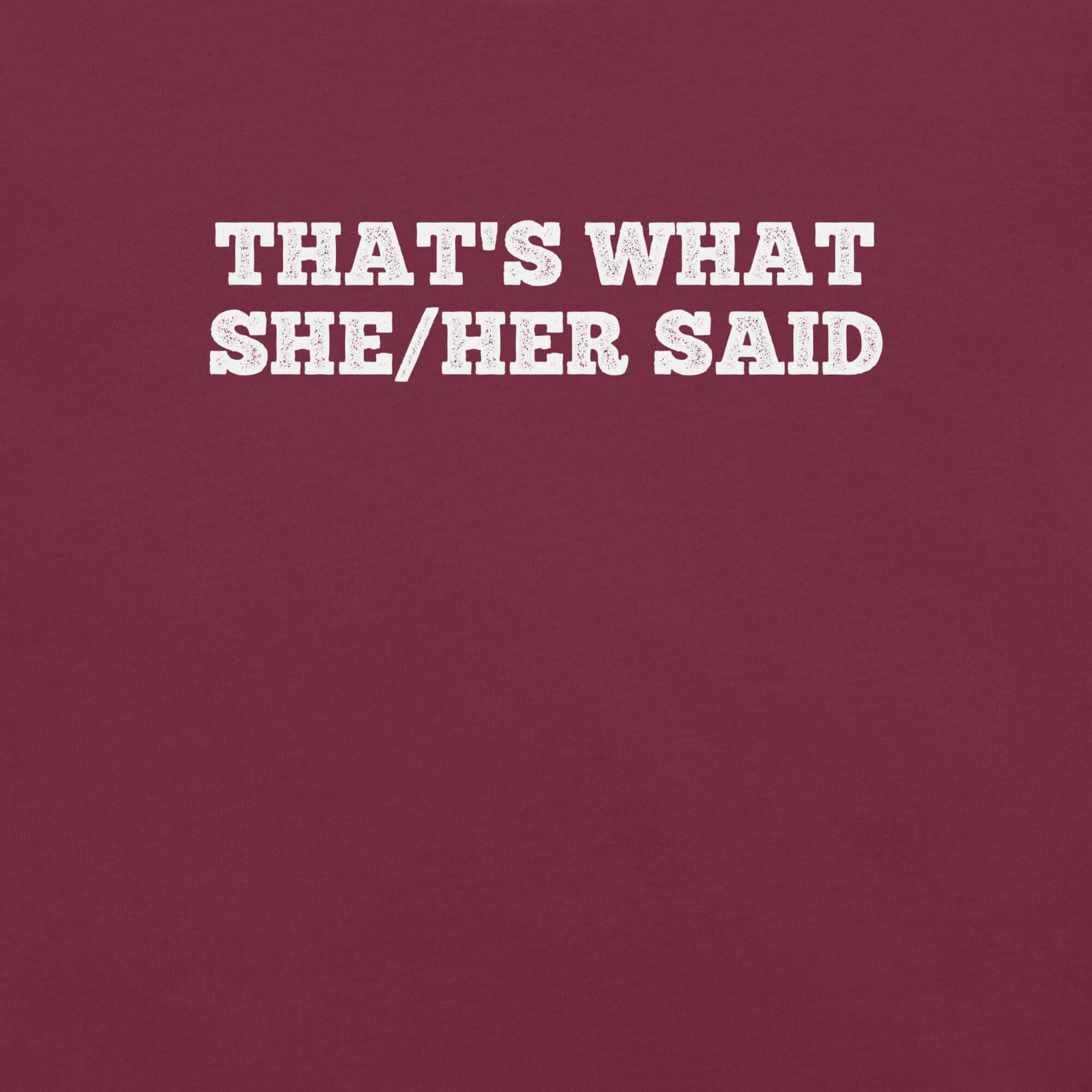 Close-up of maroon t-shirt with bold white text “THAT’S WHAT SHE/HER SAID” across the chest
