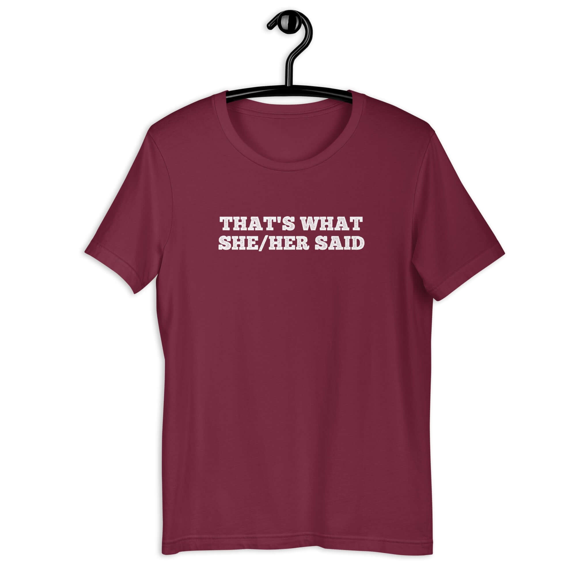 Maroon “THAT’S WHAT SHE/HER SAID” t-shirt hanging on a hanger, front design visible.      