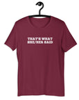 Maroon “THAT’S WHAT SHE/HER SAID” t-shirt hanging on a hanger, front design visible.      