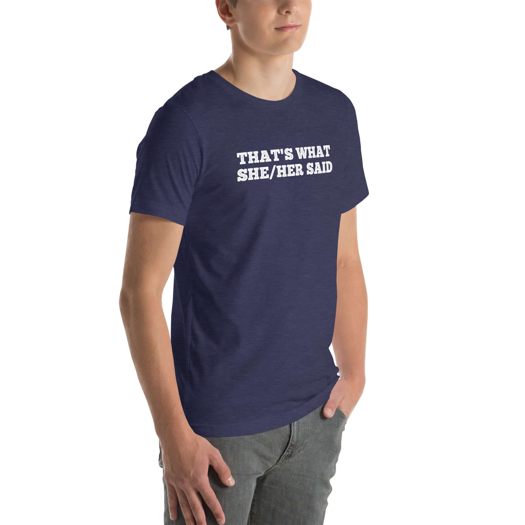 Man wearing navy “THAT’S WHAT SHE/HER SAID” t-shirt, standing casually with one hand in pocket, looking slightly to the side