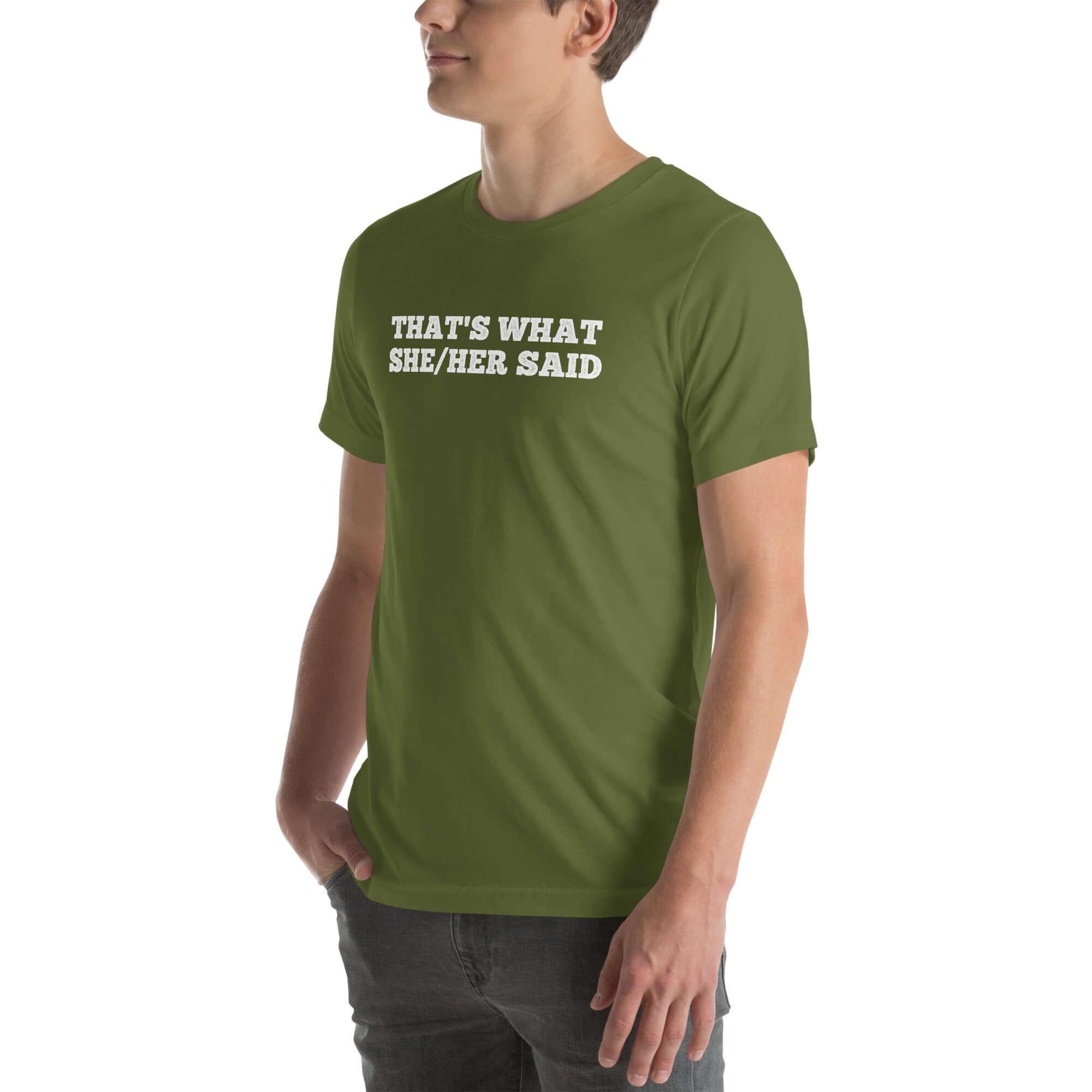 Man wearing a olive “THAT’S WHAT SHE/HER SAID” t-shirt, standing with hands in pockets, looking to the side.
