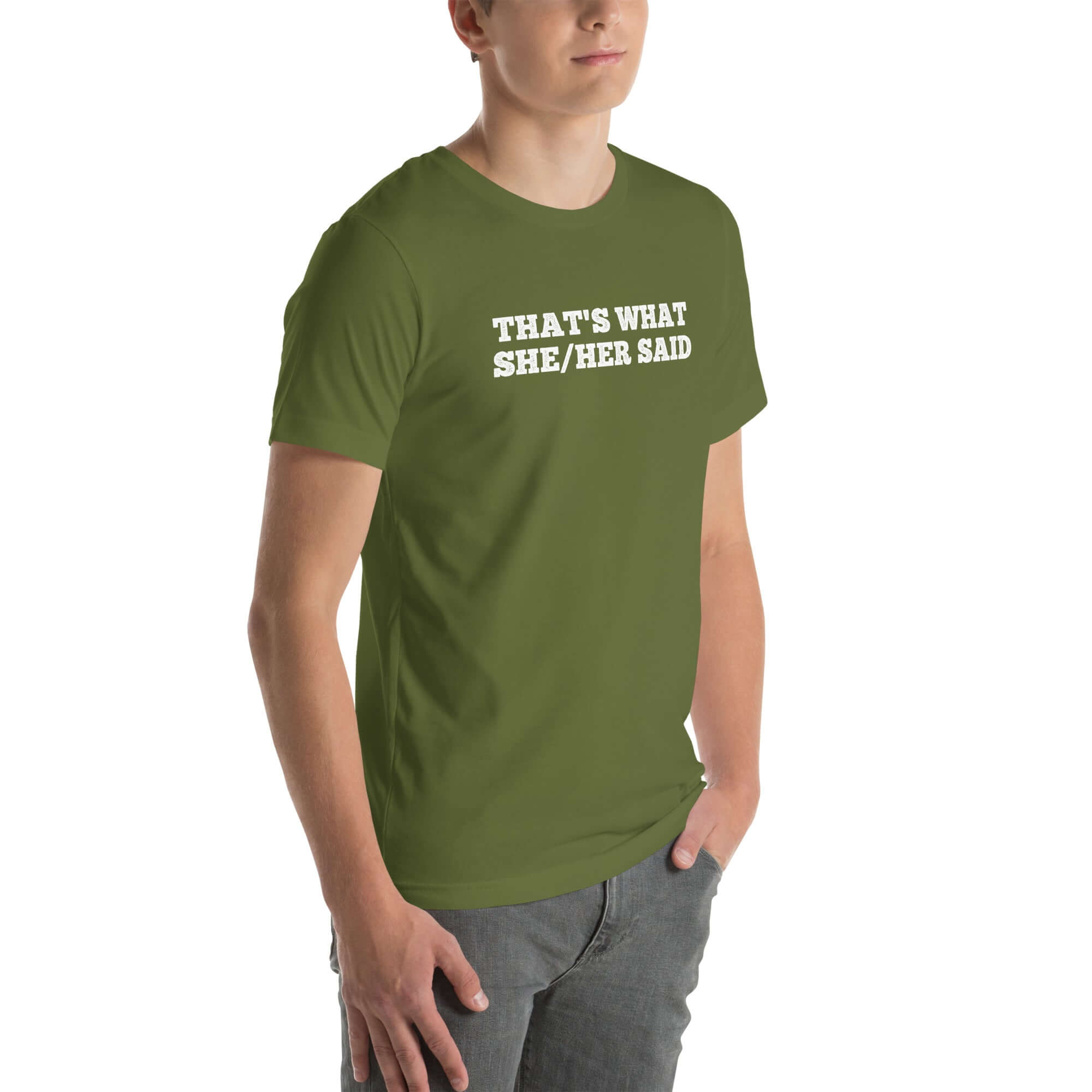 Man wearing olive “THAT’S WHAT SHE/HER SAID” t-shirt, standing casually with one hand in pocket, looking slightly to the side