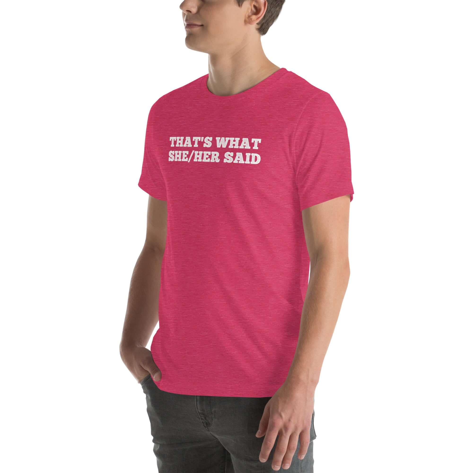 Man wearing a pink “THAT’S WHAT SHE/HER SAID” t-shirt, standing with hands in pockets, looking to the side.