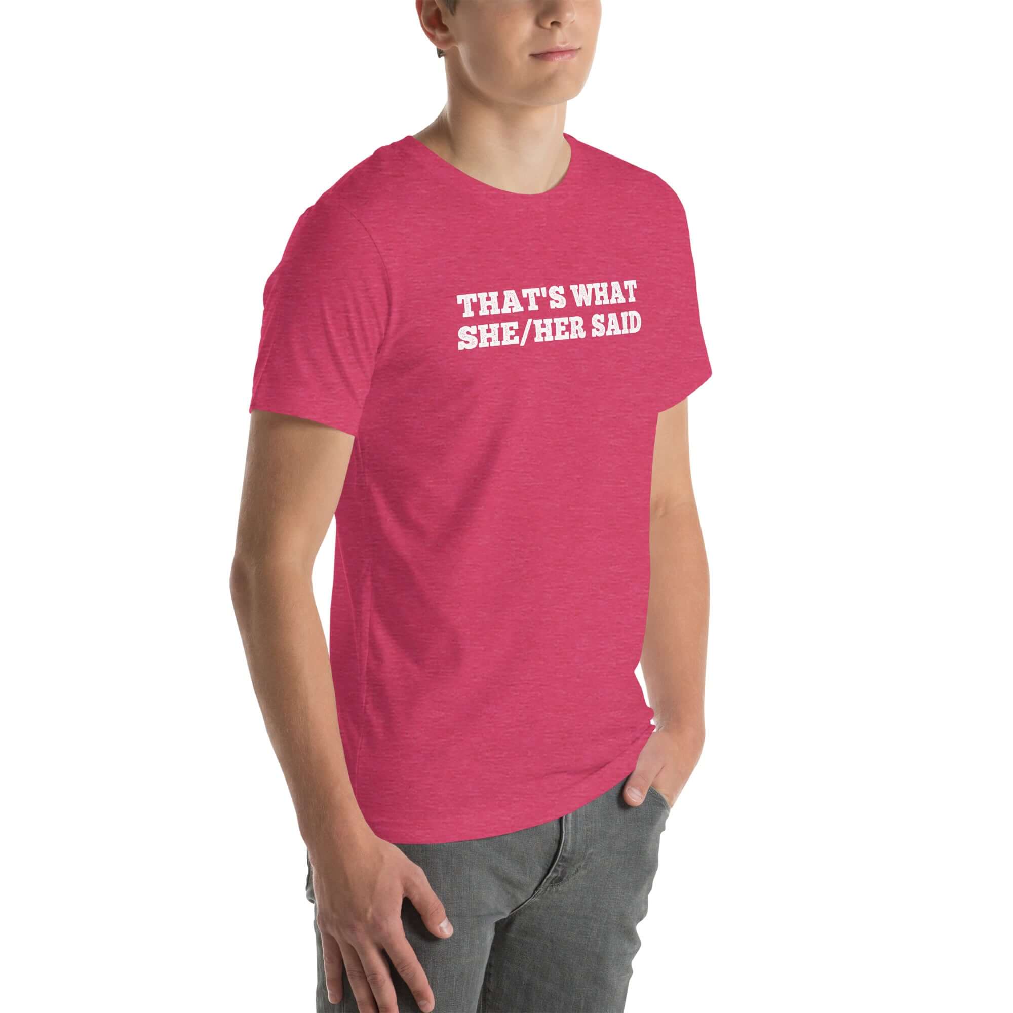 Man wearing pink “THAT’S WHAT SHE/HER SAID” t-shirt, standing casually with one hand in pocket, looking slightly to the side