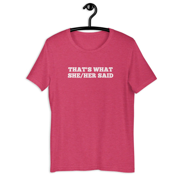 Pink “THAT’S WHAT SHE/HER SAID” t-shirt hanging on a hanger, front design visible.      