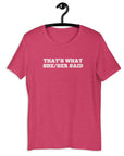 Pink “THAT’S WHAT SHE/HER SAID” t-shirt hanging on a hanger, front design visible.      