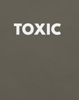 Man wearing army “TOXIC” t-shirt, standing with hands in pockets, looking slightly to the side.