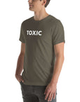 Man wearing army “TOXIC” t-shirt, standing sideways with hands in pockets, looking off to the side.
