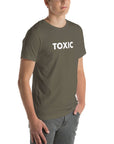Man wearing army “TOXIC” t-shirt, standing with hands in pockets, looking slightly to the side.