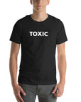 Man wearing black “TOXIC” t-shirt, standing straight with hands relaxed by pockets, facing forward.