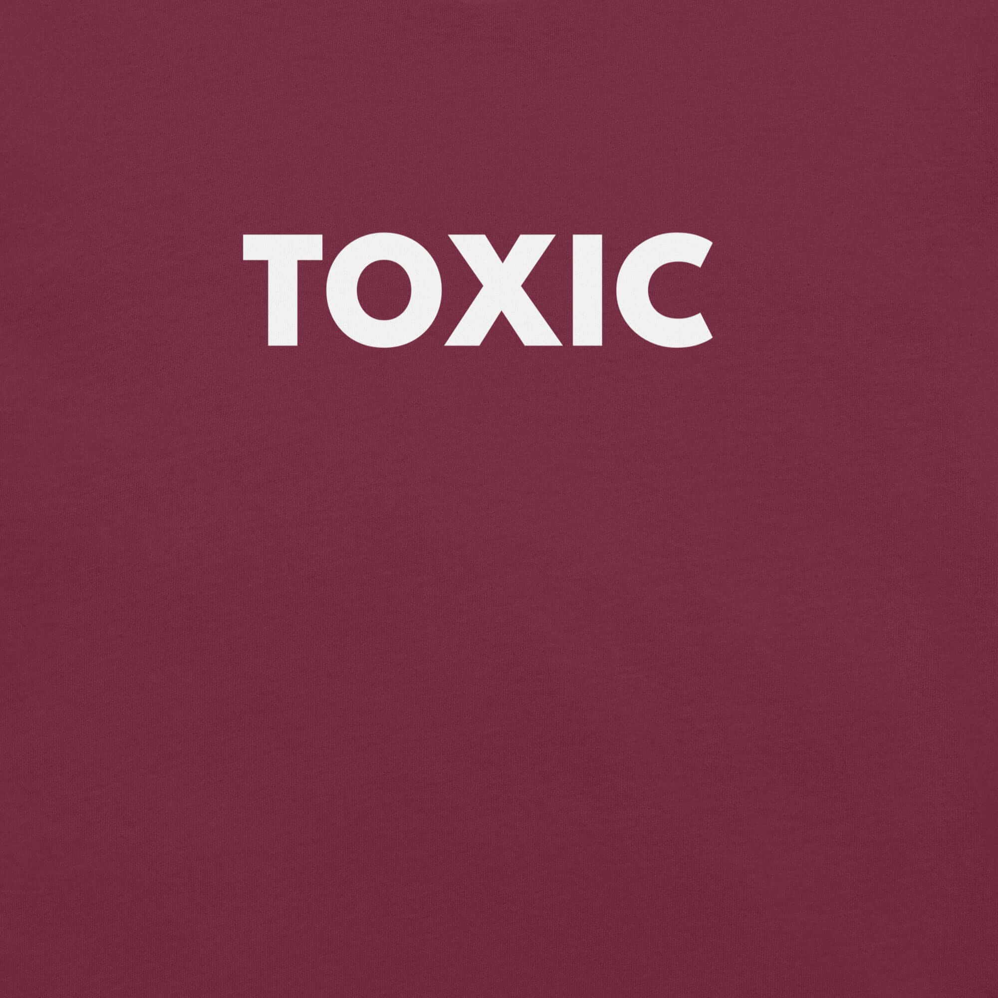 Man wearing maroon “TOXIC” t-shirt, standing with hands in pockets, looking slightly to the side.
