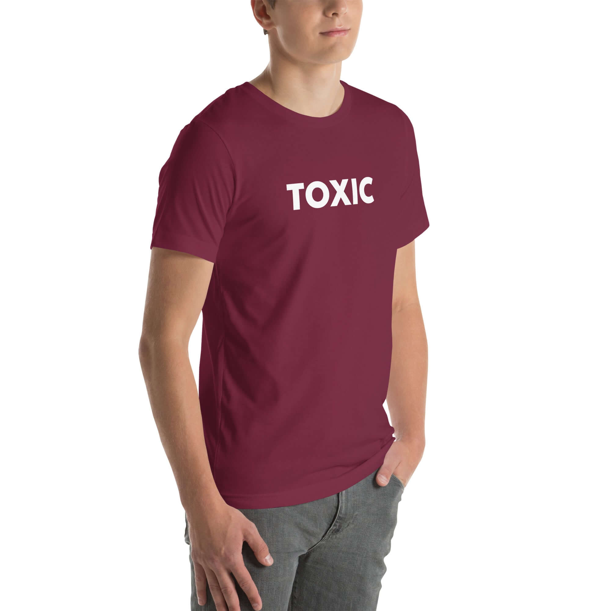 Man wearing maroon “TOXIC” t-shirt, standing with hands in pockets, looking slightly to the side.
