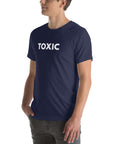 Man wearing navy “TOXIC” t-shirt, standing sideways with hands in pockets, looking off to the side.
