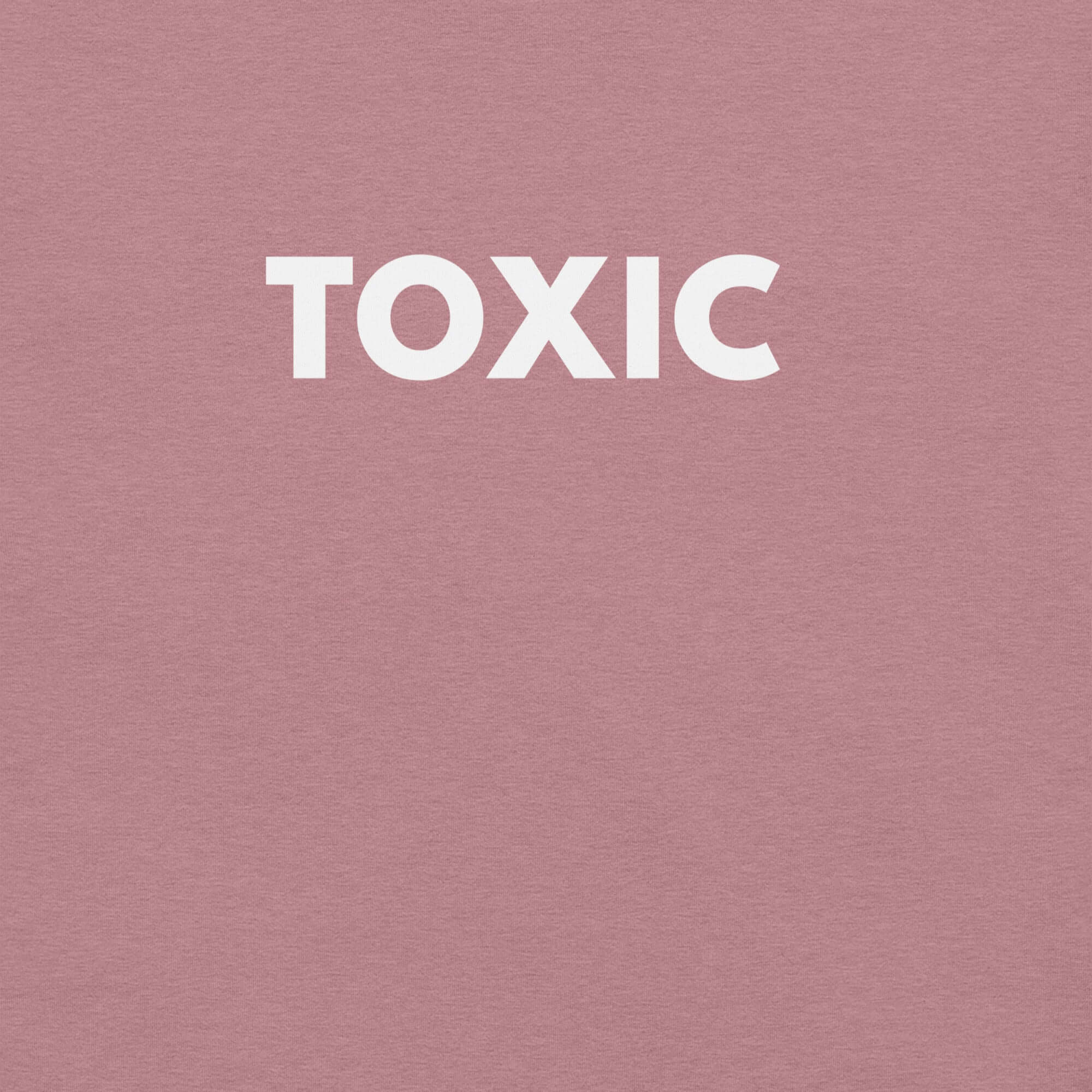 Man wearing orchid “TOXIC” t-shirt, standing with hands in pockets, looking slightly to the side.