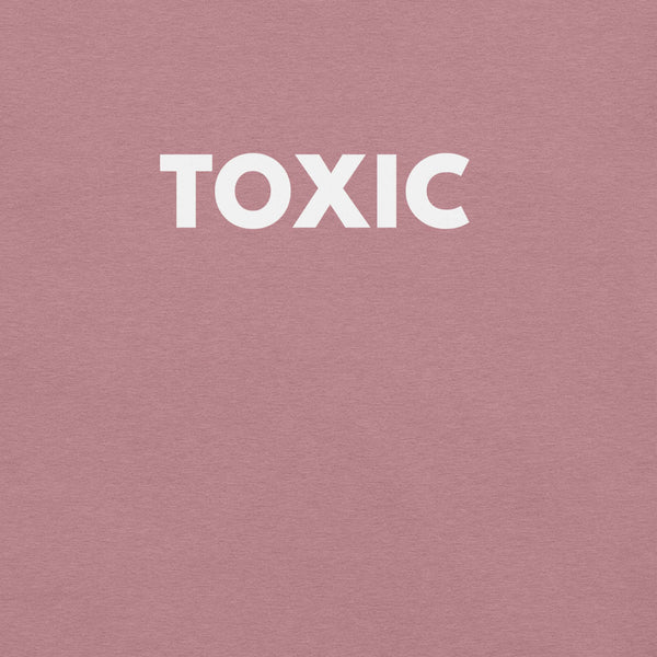 Man wearing orchid “TOXIC” t-shirt, standing with hands in pockets, looking slightly to the side.