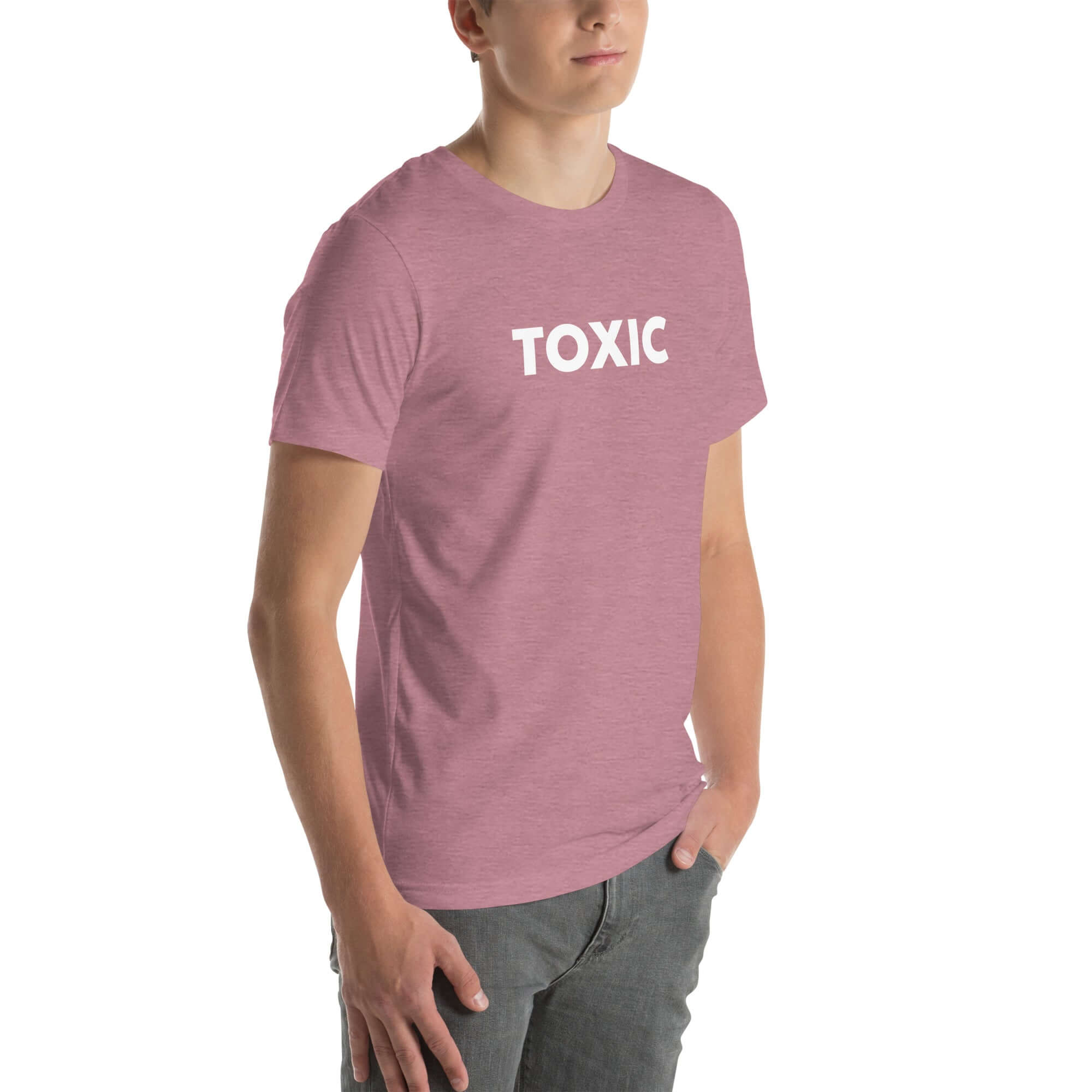 Man wearing orchid “TOXIC” t-shirt, standing with hands in pockets, looking slightly to the side.