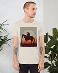 Unisex t-shirt featuring cowboy graphic with sunset, worn by model in stylish room with plants. Perfect blend of comfort and style.