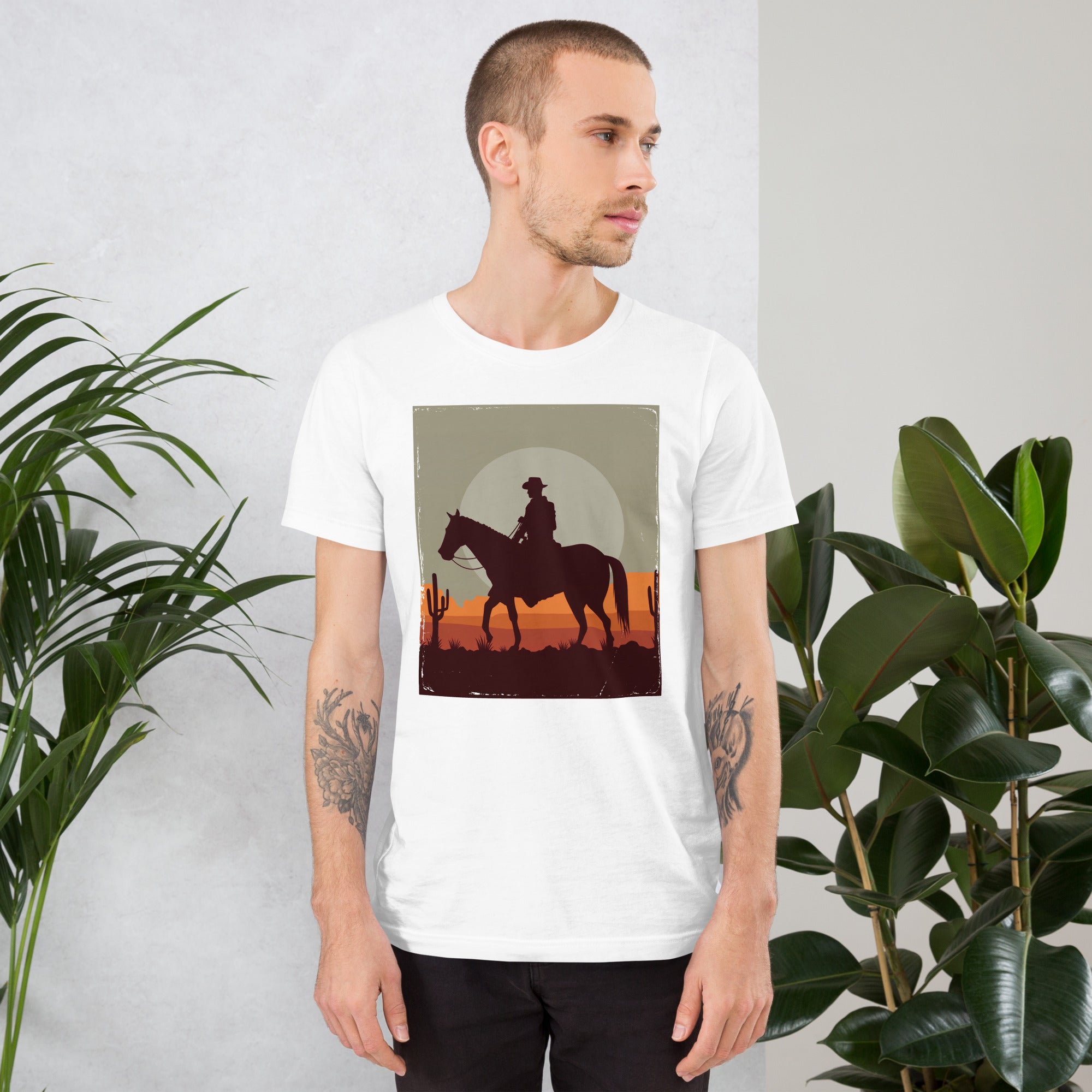 Model wearing a unisex t-shirt with a cowboy graphic design against a sunset background, surrounded by greenery.