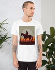 Model wearing a unisex t-shirt with a cowboy graphic design against a sunset background, surrounded by greenery.